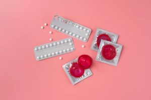 An image of barrier contraceptives and oral contraceptive pills scattered against a pink background