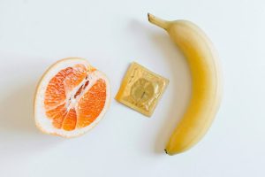 Image of fruits (orange and banana) and a condom against a white background